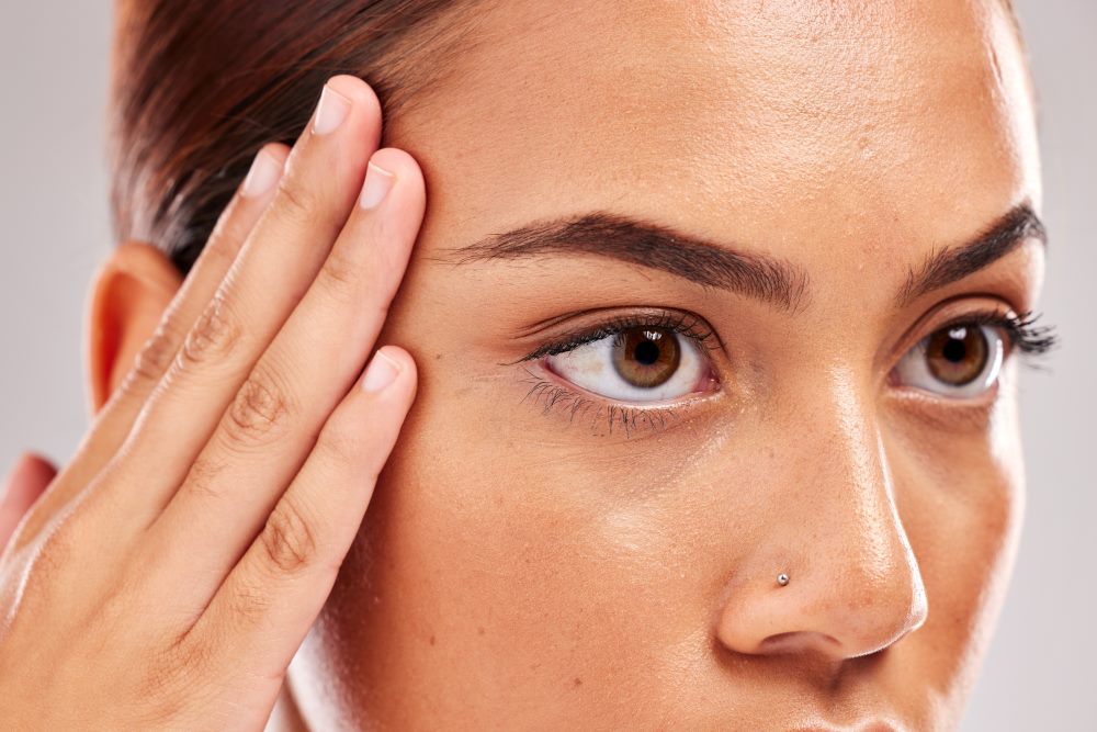 A woman holding the side of her face near her eyebrows.