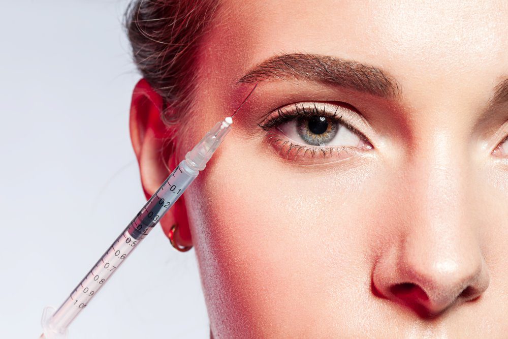 Close-up of a woman doing an injection under the eyebrow.