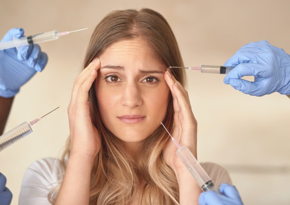 Anxious young woman with botox needles pointed around at her face.