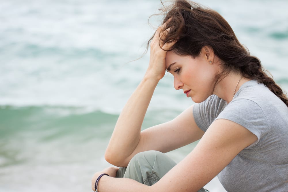 Woman sitting at beachside having anxiety due to bulging veins