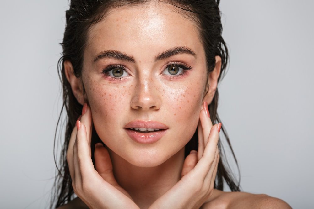 A brunette woman holding her hands up to the cheekbones of her face.