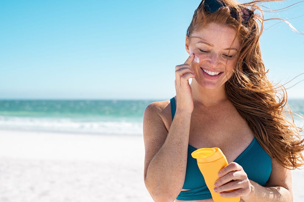Woman wearing sunscreen at the beach avoiding sunspots and sun damage
